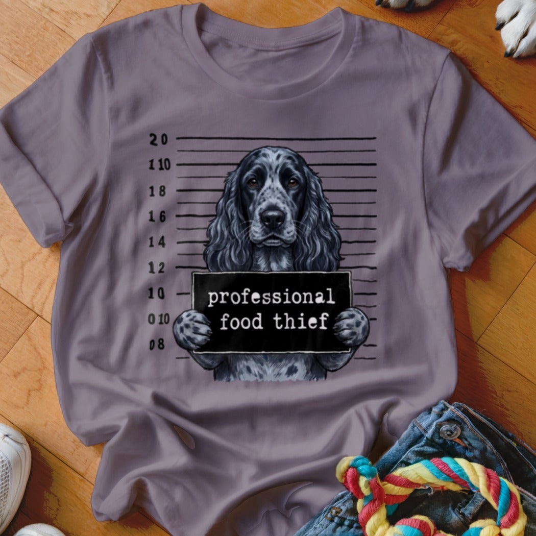 Cocker spaniel mugshot with "professional food thief" sign on a t-shirt.