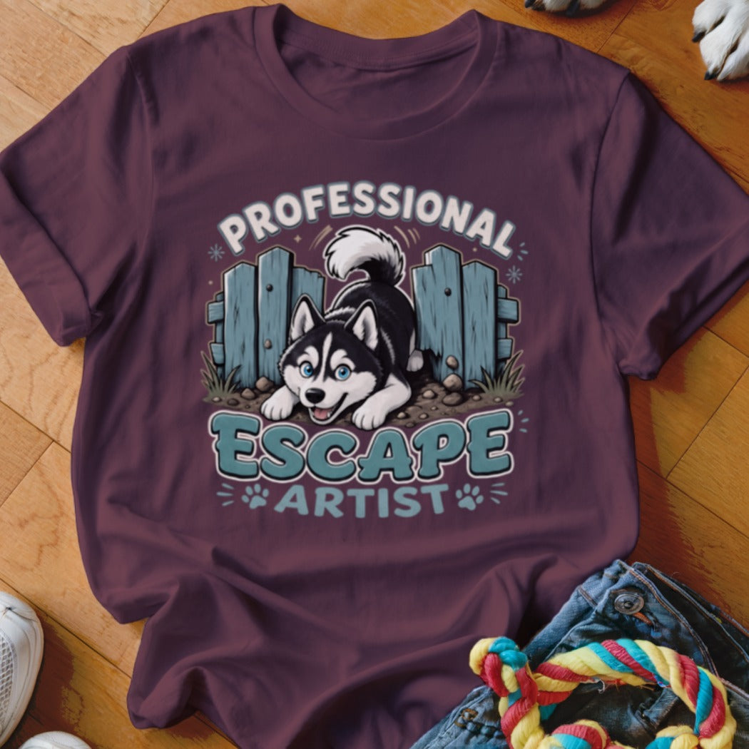 T-shirt graphic of a husky escaping a blue fence, reading "Professional Escape Artist".