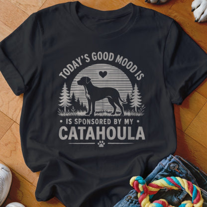 A black t-shirt printed with a graphic featuring a dog silhouette, pine trees, and text reading Today Good Mood Is Sponsored By My Catahoula.