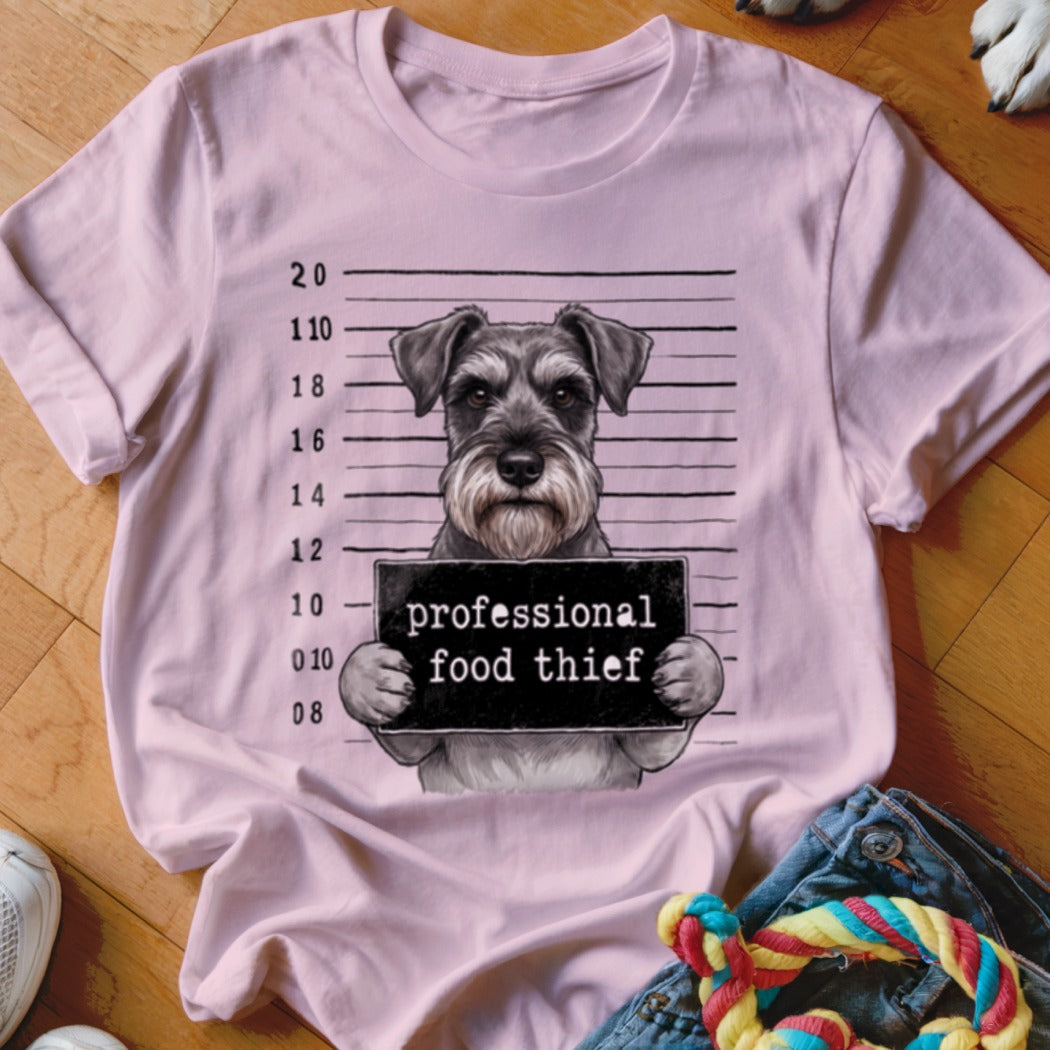 Schnauzer dog in mugshot holding "professional food thief" sign on a pink t-shirt.