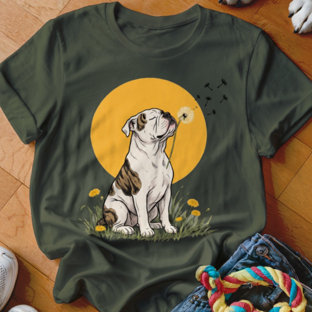 A dark green t-shirt featuring an illustration of a bulldog blowing on a dandelion against a yellow sun.