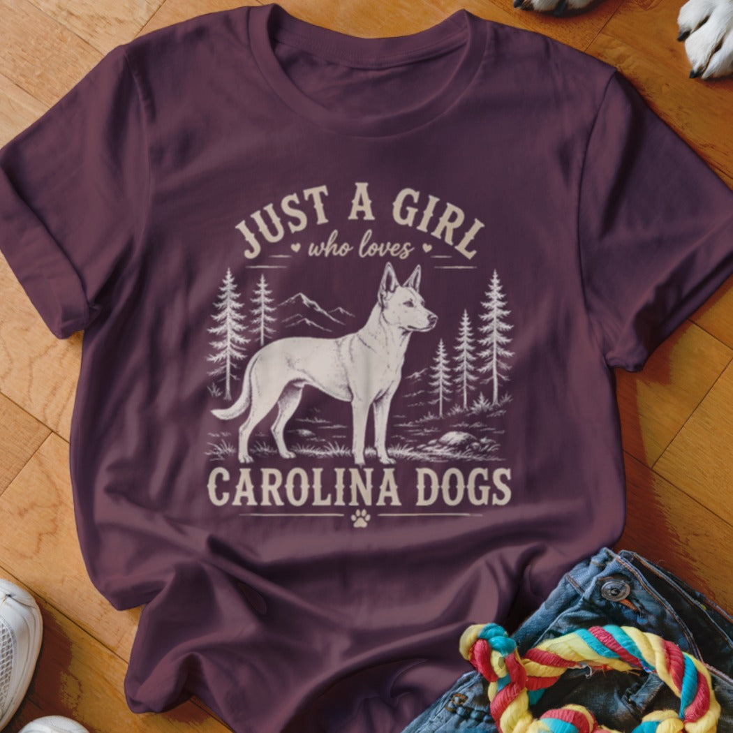 Burgundy t-shirt with graphic: white dog, trees, mountains, and text "Just a girl who loves Carolina Dogs".