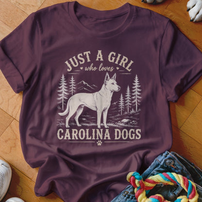 Burgundy t-shirt with graphic: white dog, trees, mountains, and text "Just a girl who loves Carolina Dogs".
