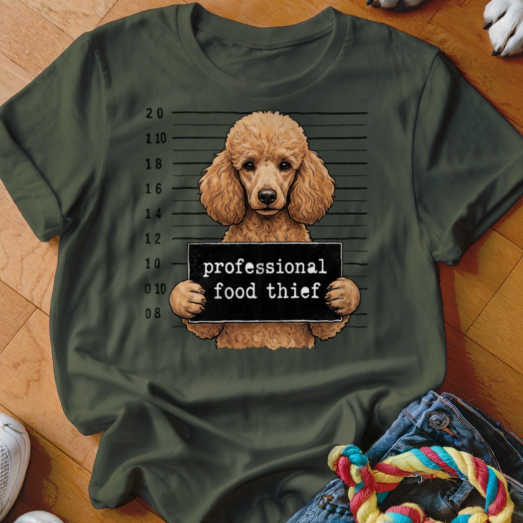 Brown poodle holds sign reading "professional food thief" on dark green t-shirt.