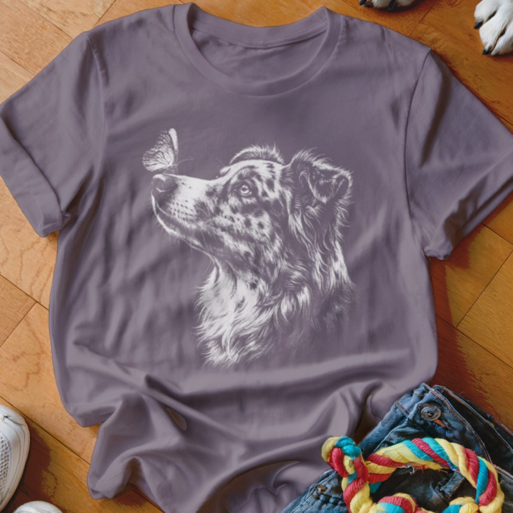 A dusty purple t-shirt features a white line drawing of an Australian Shepherd looking at a butterfly on its nose.