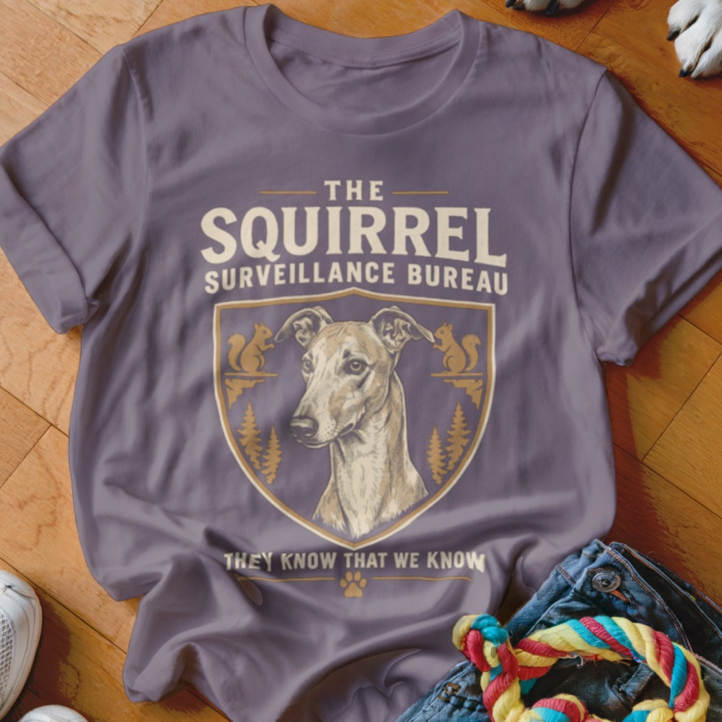 A purple t-shirt featuring a dog graphic, crest, and text that reads The Squirrel Surveillance Bureau.