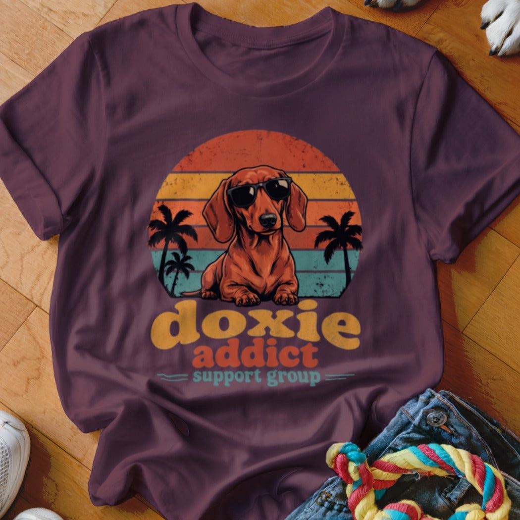 A plum t-shirt featuring a retro graphic of a dachshund in sunglasses with the text "doxie addict support group."