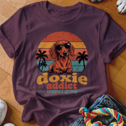A plum t-shirt featuring a retro graphic of a dachshund in sunglasses with the text "doxie addict support group."