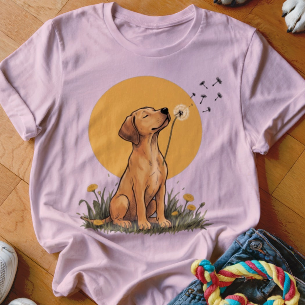 Light pink crewneck t-shirt featuring an illustration of a golden puppy blowing dandelion seeds against a yellow circle background.