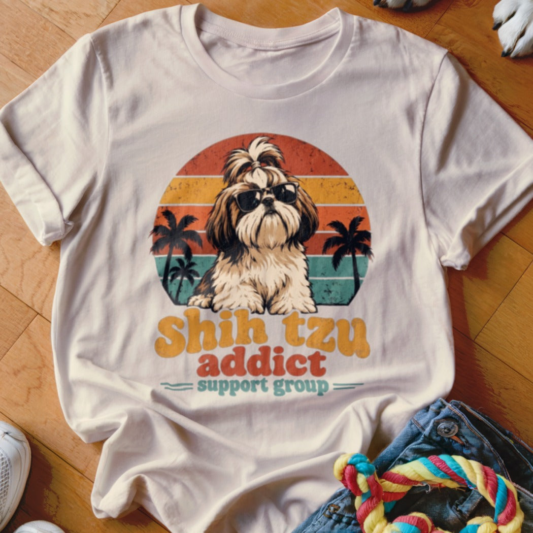 Light-colored t-shirt featuring a retro graphic of a Shih Tzu wearing sunglasses against a sunset and palm trees.