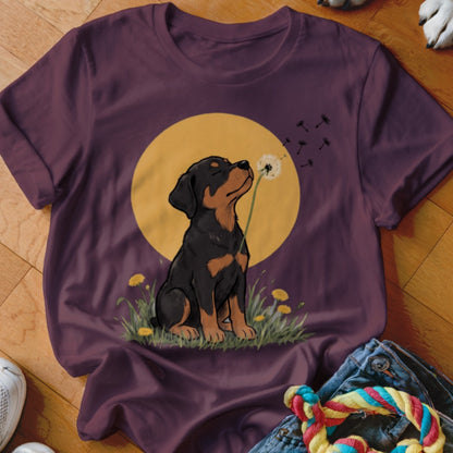 Maroon t-shirt featuring an illustrated Rottweiler puppy blowing dandelion seeds against a yellow circle background.