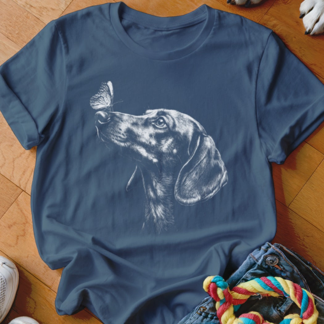 A dark blue short-sleeved t-shirt featuring a white sketch of a dachshund looking at a butterfly.