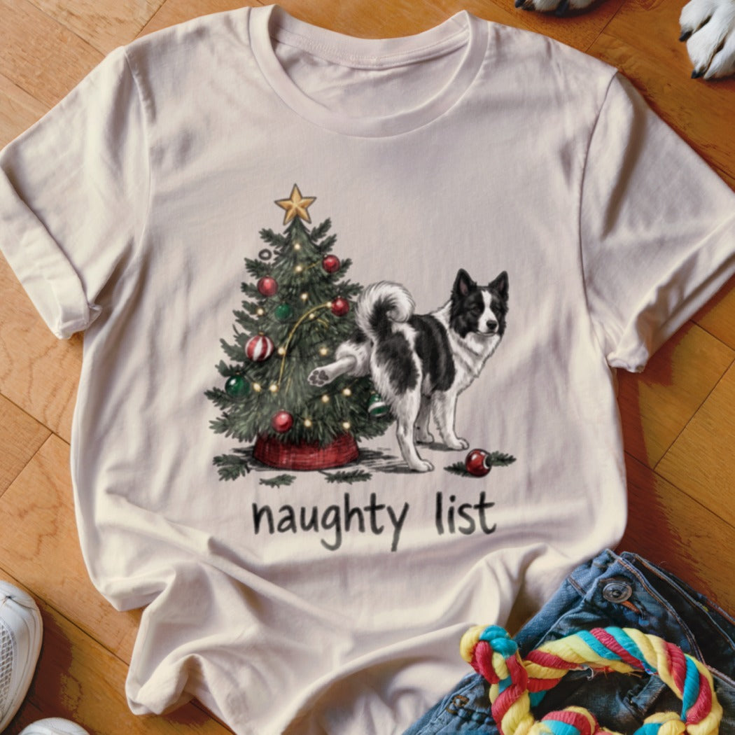 A light pink t-shirt featuring a graphic of a dog lifting its leg against a Christmas tree, with the text "naughty list".