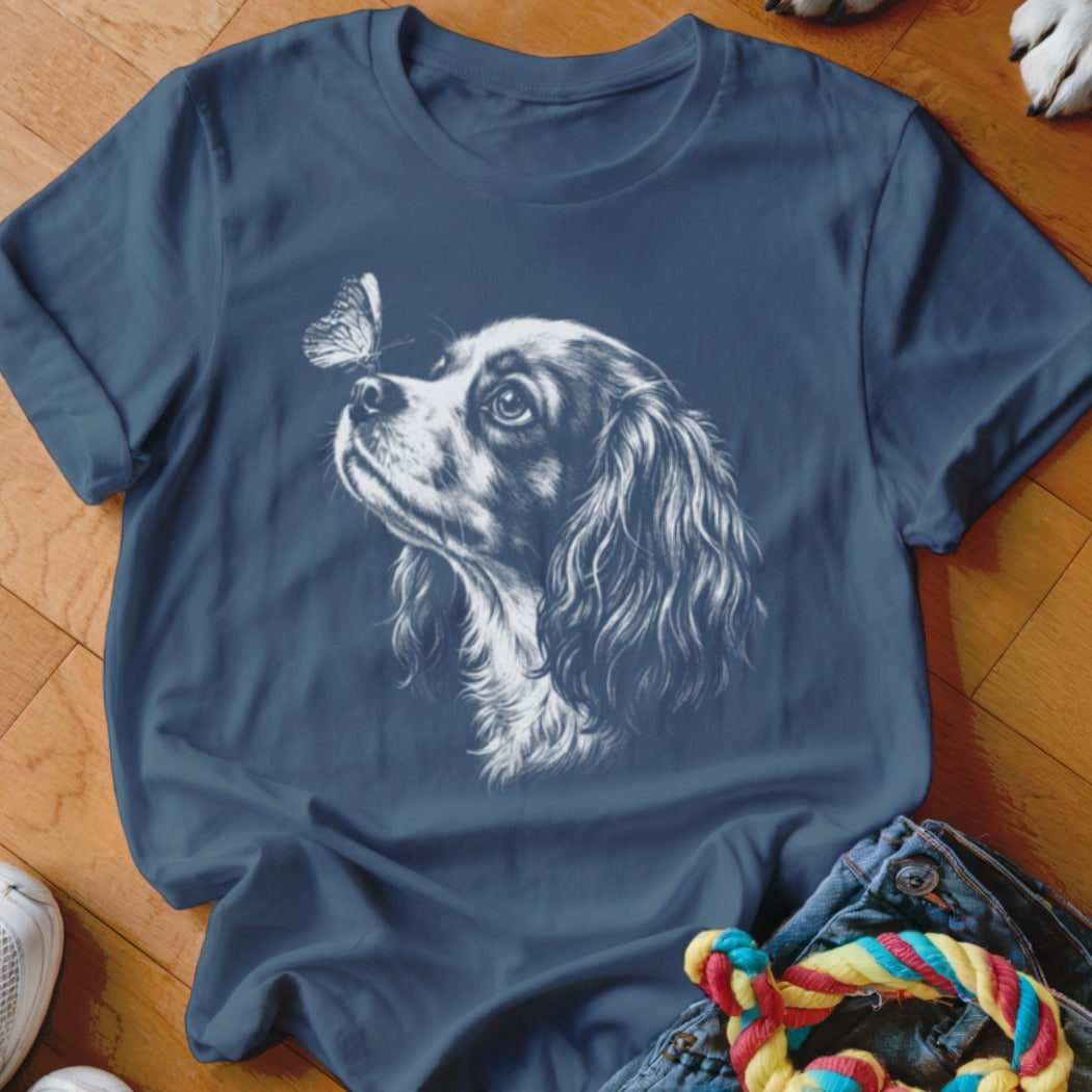 A dark blue crewneck t-shirt featuring a white line drawing of a spaniel looking at a butterfly on its nose.