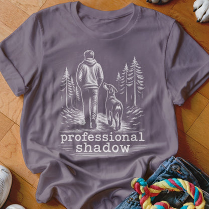 Gray t-shirt with a sketch of a person and dog walking on a path, text reads "professional shadow".