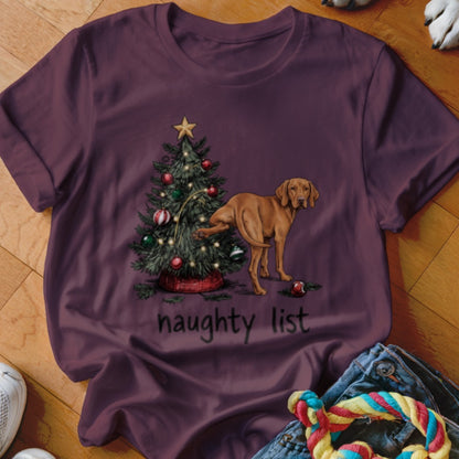 Maroon t-shirt featuring an illustration of a brown dog lifting its leg against a Christmas tree, with the text naughty list.