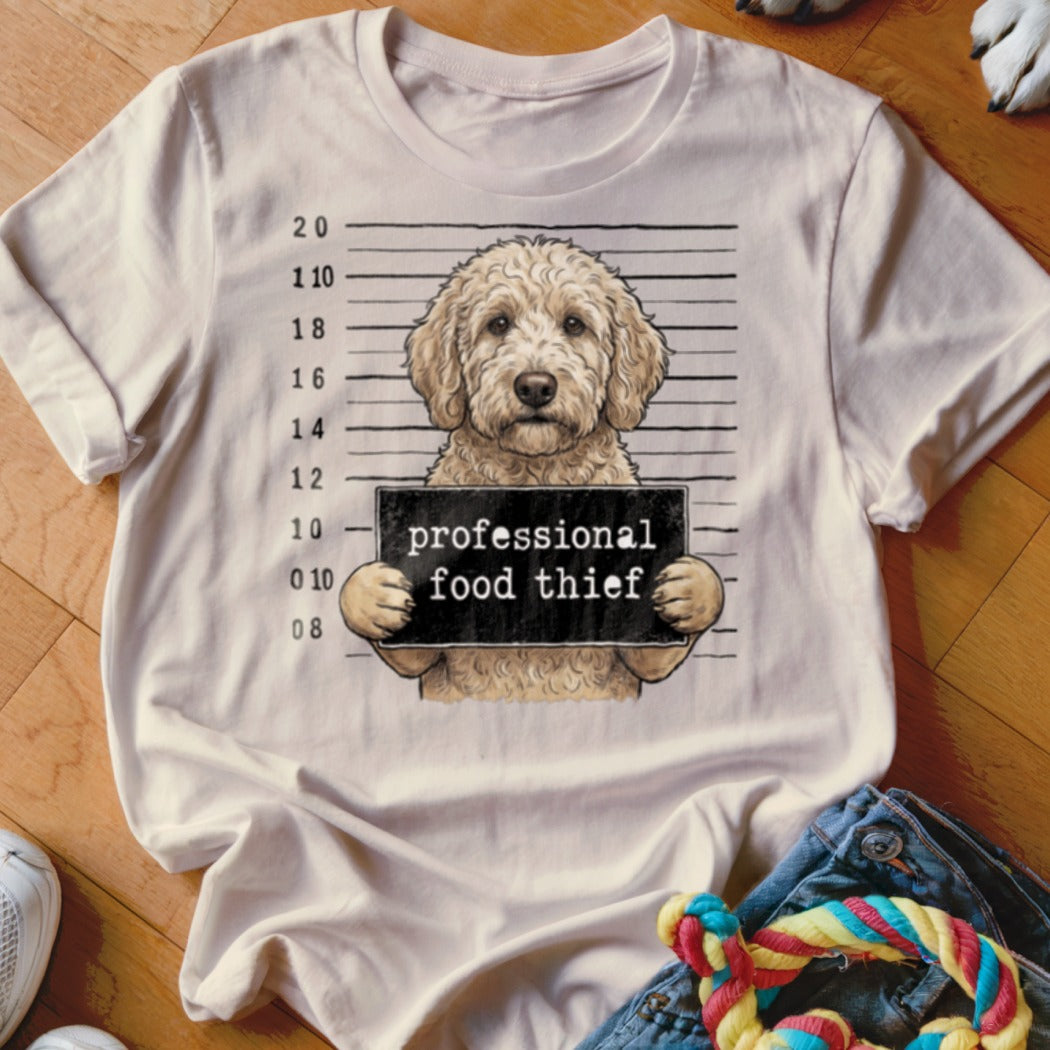 A goldendoodle dog holding a sign that says "professional food thief".