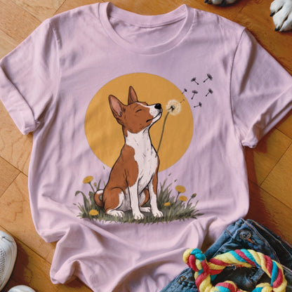 A light pink t-shirt displays a graphic of a brown and white dog blowing dandelion seeds.
