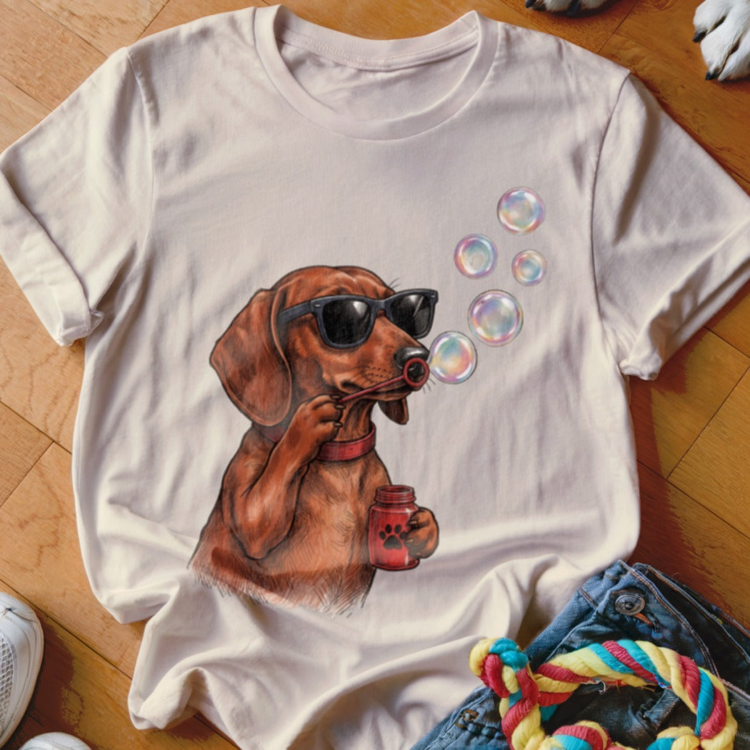 Beige t-shirt featuring a cartoon dachshund wearing sunglasses and blowing colorful bubbles.