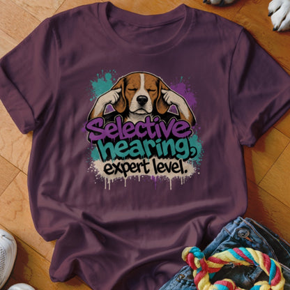 Beagle dog with paws over ears on a purple t-shirt, text reads "Selective hearing! expert level."