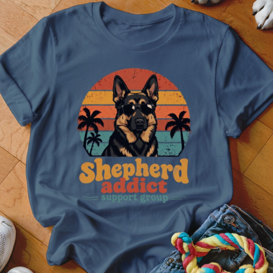 Blue t-shirt featuring a German Shepherd in sunglasses against a retro sunset and palm tree graphic with text reading Shepherd Addict Support Group.