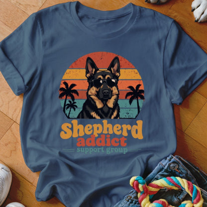 Blue t-shirt featuring a German Shepherd in sunglasses against a retro sunset and palm tree graphic with text reading Shepherd Addict Support Group.