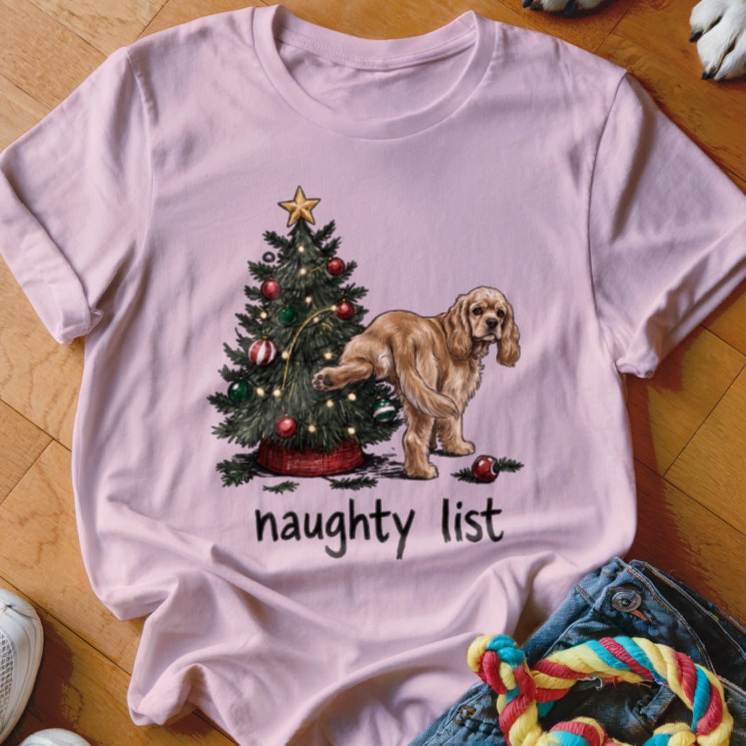 Pink t-shirt with a tan dog next to a decorated Christmas tree and the text "naughty list".