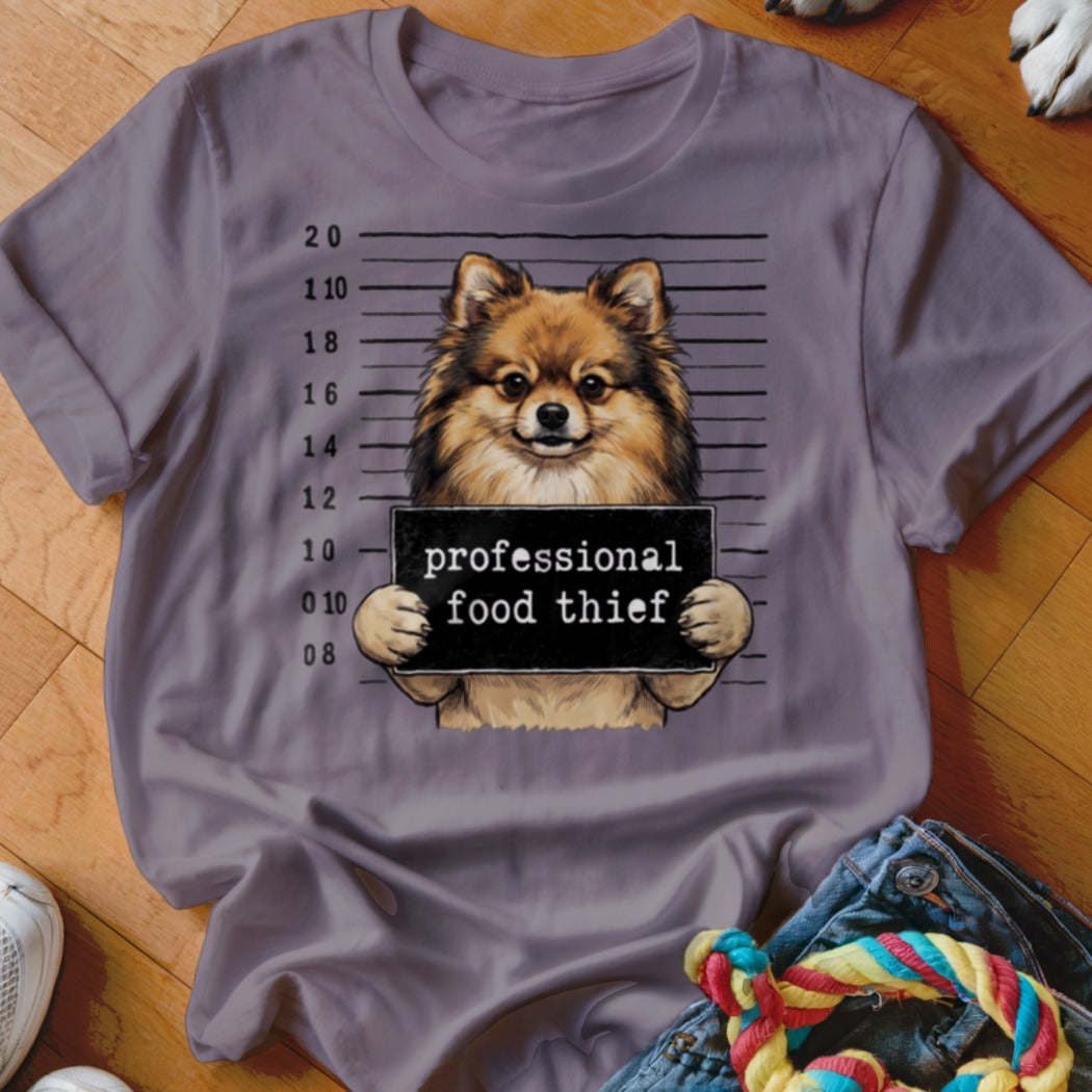 Pomeranian dog in mugshot holding "professional food thief" sign.