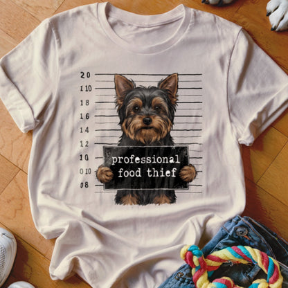 Yorkshire terrier in mugshot holding sign saying "professional food thief."