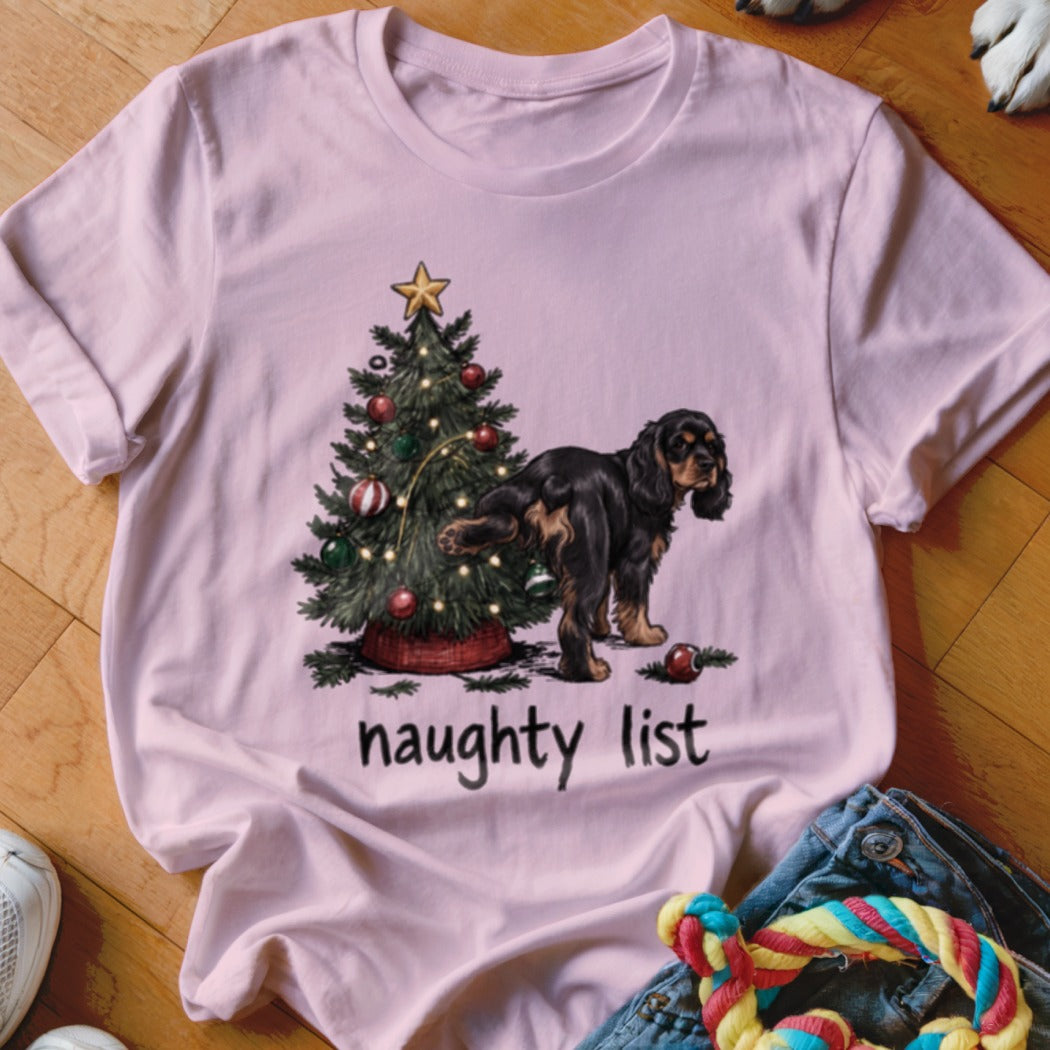 Pink t-shirt with illustration of dog near Christmas tree and text "naughty list".