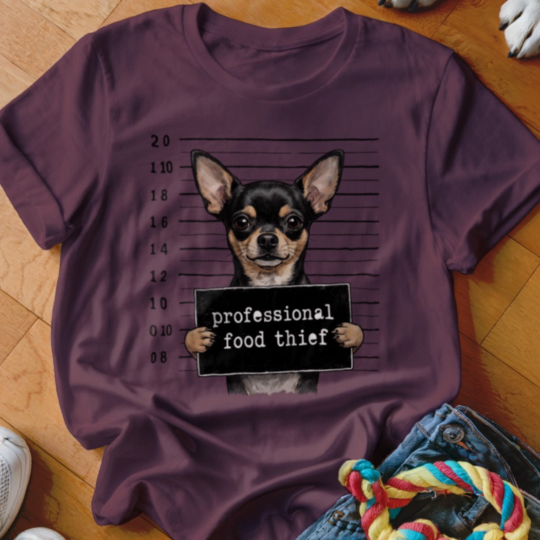 Chihuahua mugshot with "professional food thief" sign on a maroon t-shirt.