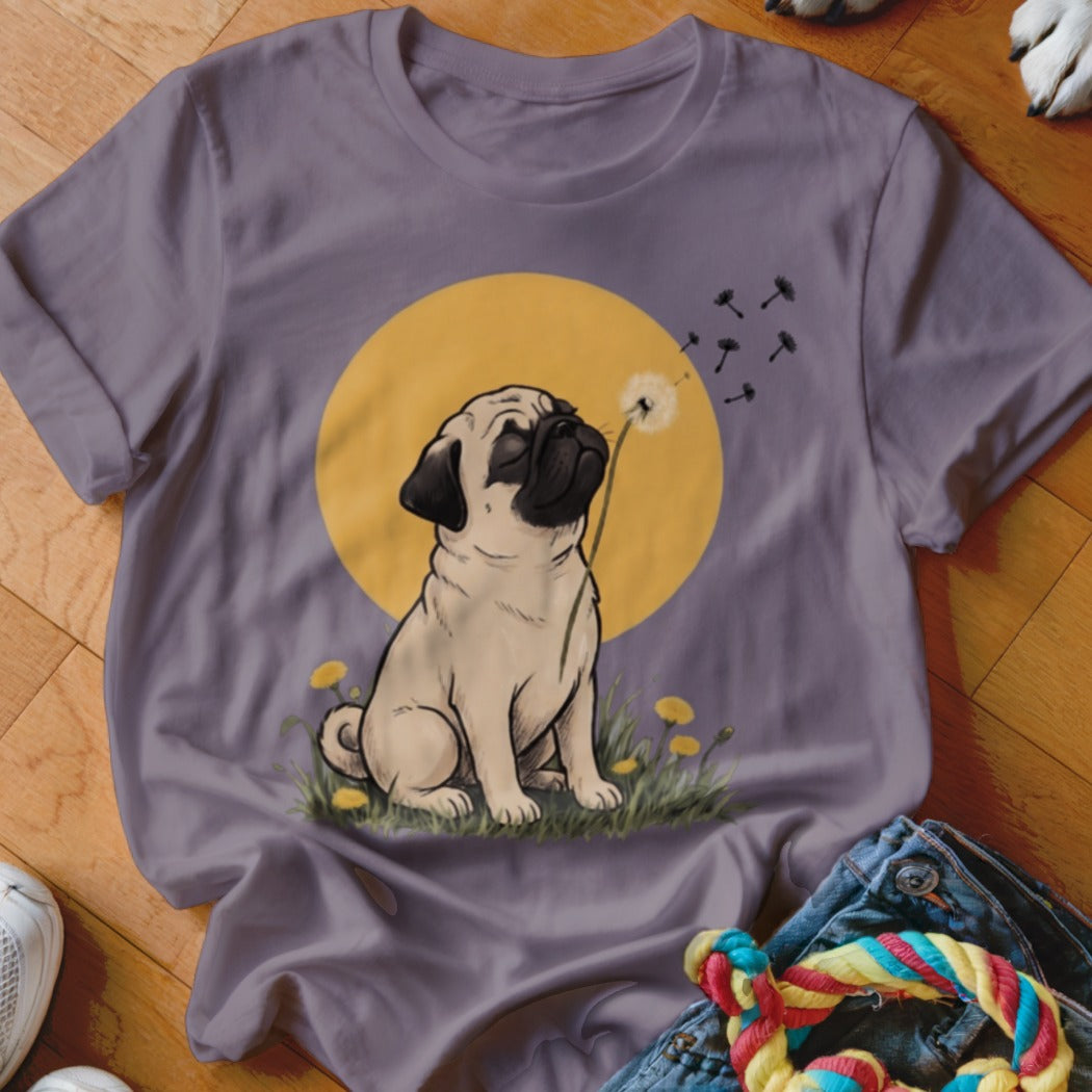 A purple t-shirt featuring an illustration of a pug blowing dandelion seeds against a yellow sun.
