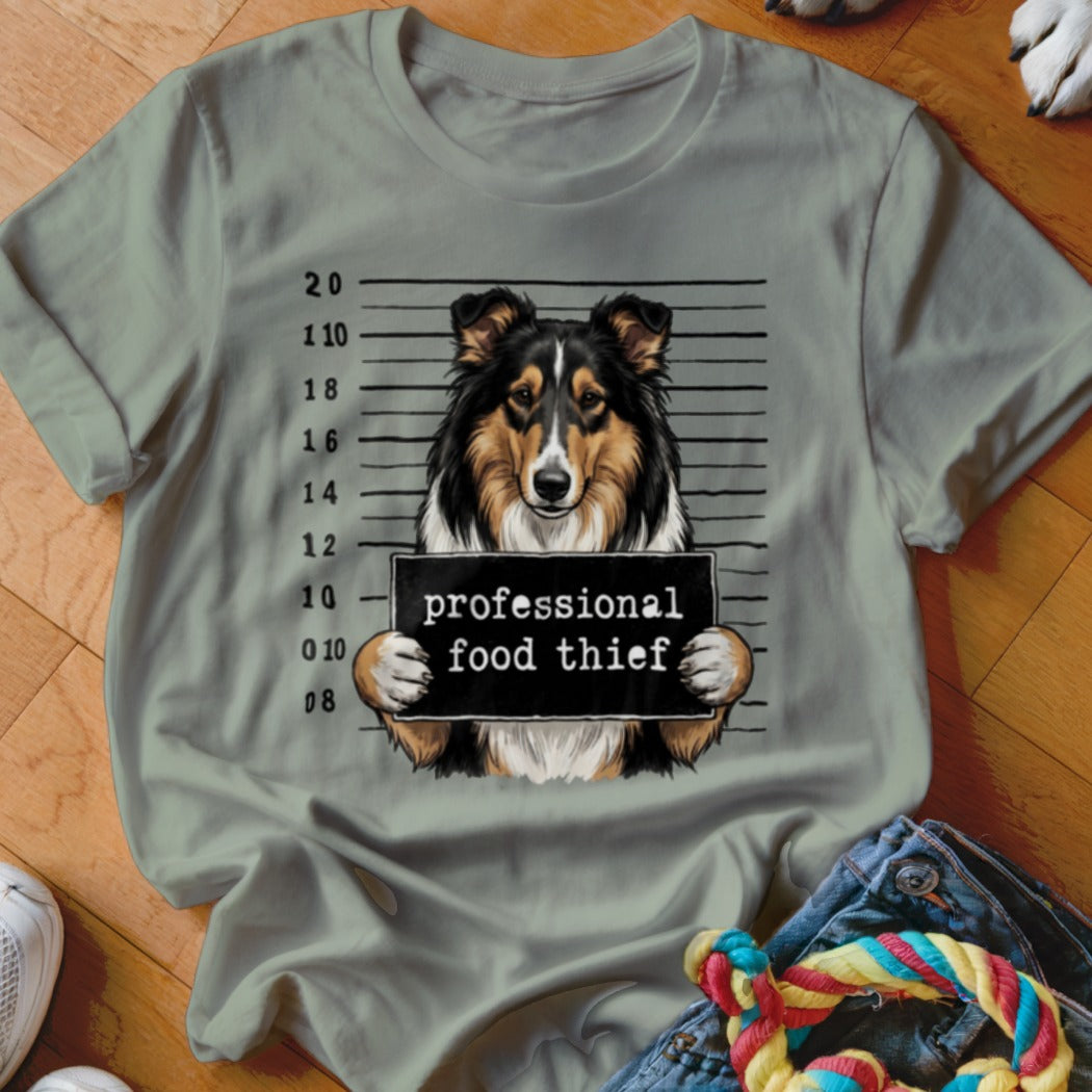 Collie dog mugshot with "professional food thief" sign on grey t-shirt.