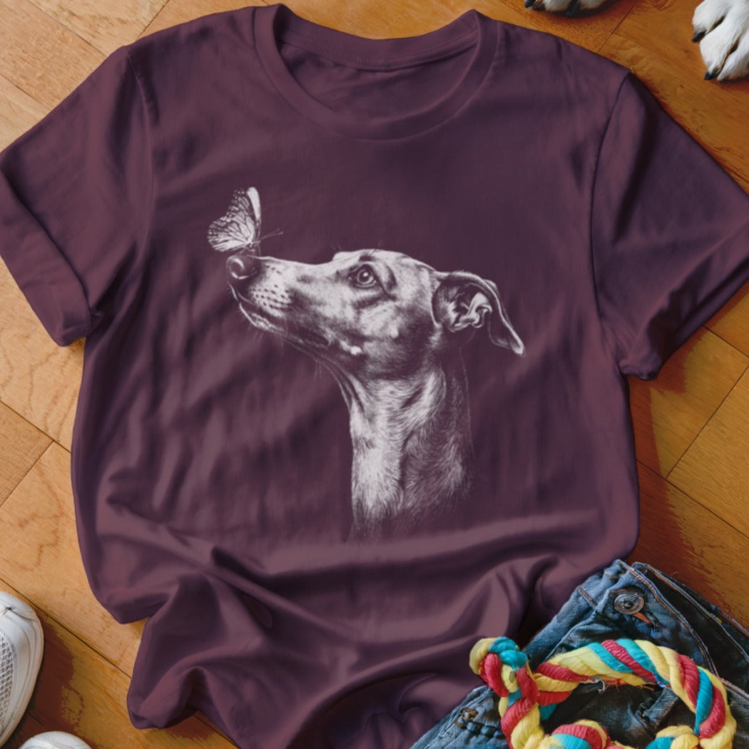A dark purple short-sleeved t-shirt featuring a white line drawing of a dog looking at a butterfly on its nose.