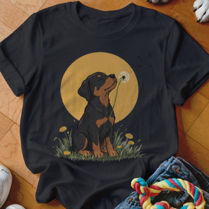 Black t-shirt featuring an illustration of a Rottweiler puppy blowing dandelion seeds against a yellow circle background.