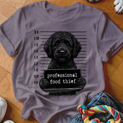 Black poodle dog holding a "professional food thief" sign on a mugshot background.