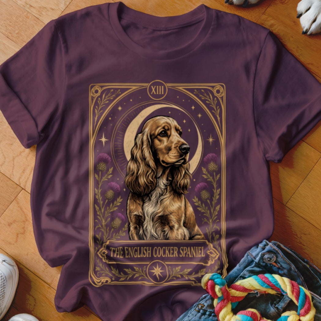 A maroon t-shirt featuring a tarot card style graphic of an English Cocker Spaniel with thistles and a crescent moon.