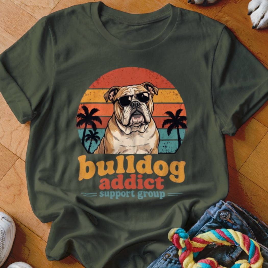 An olive green t-shirt with a vintage-style graphic of a bulldog wearing sunglasses against a sunset.