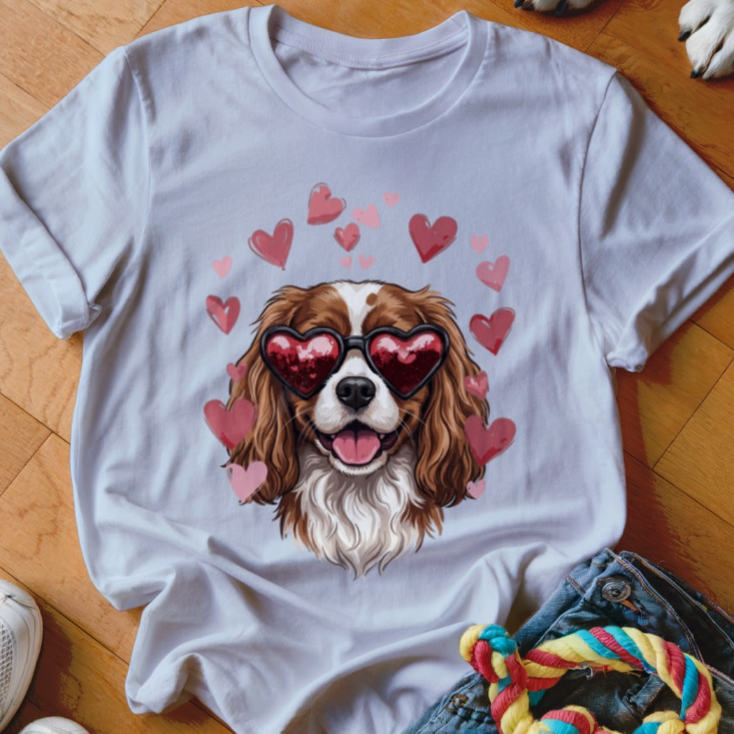 White t-shirt featuring an illustration of a Cavalier King Charles Spaniel wearing heart-shaped sunglasses surrounded by floating pink hearts.