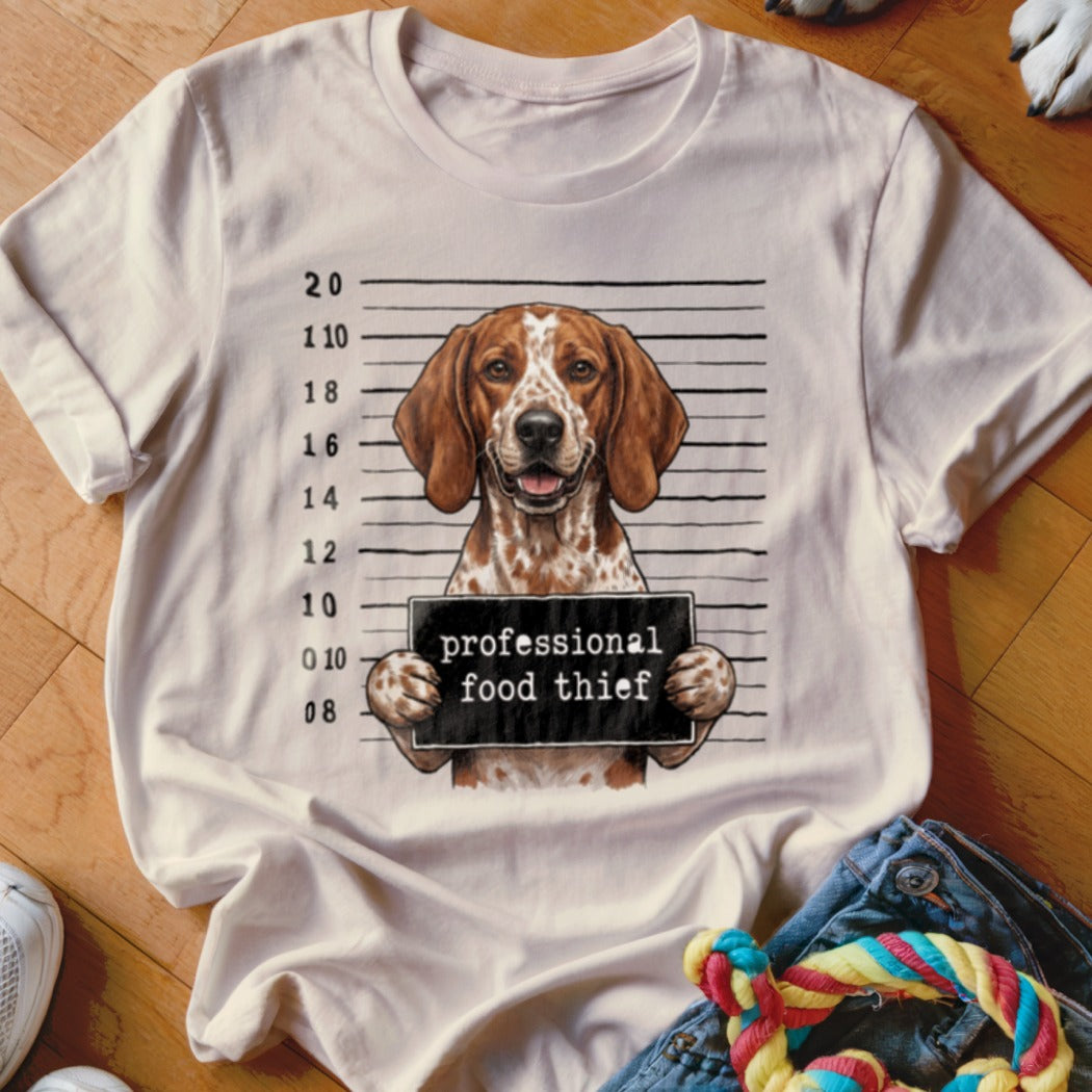 Beagle dog mugshot with "professional food thief" sign on t-shirt.