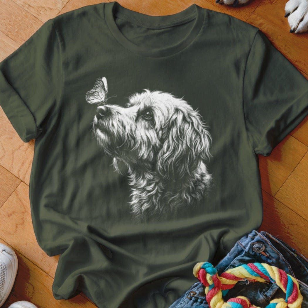 Dark green t-shirt featuring a white sketched graphic of a fluffy dog looking at a butterfly on its nose.