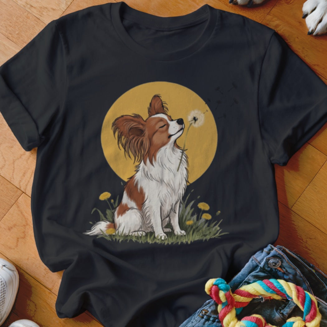 Black t-shirt featuring an illustration of a Papillon dog blowing dandelion seeds against a yellow sun.