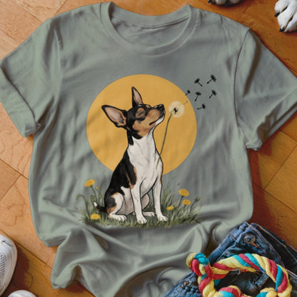 Sage green t-shirt featuring an illustration of a black and white dog blowing dandelion seeds against a yellow sun.