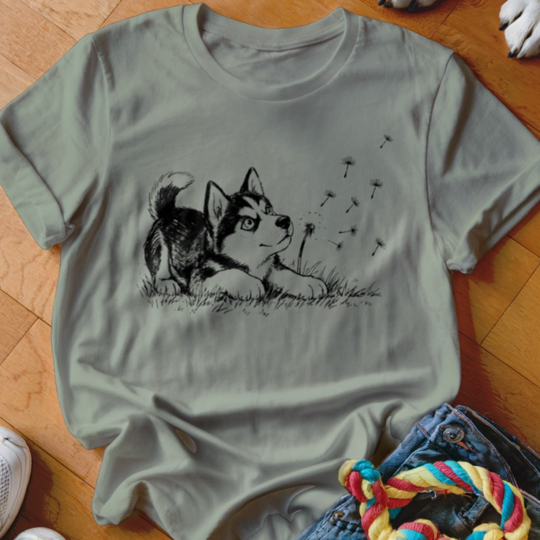 Sage green crewneck t-shirt featuring a black line art graphic of a puppy watching dandelion seeds.