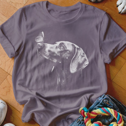 A purple t-shirt featuring a white graphic of a dog looking at a butterfly on its nose.