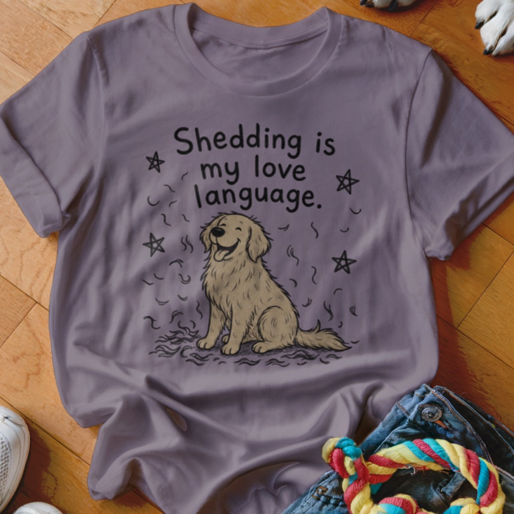 A dusty purple t-shirt features a smiling golden retriever surrounded by floating fur and stars, with the text Shedding is my love language.