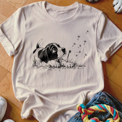 A light pink crewneck t-shirt featuring a black and white sketch of a puppy watching dandelion seeds blow away.