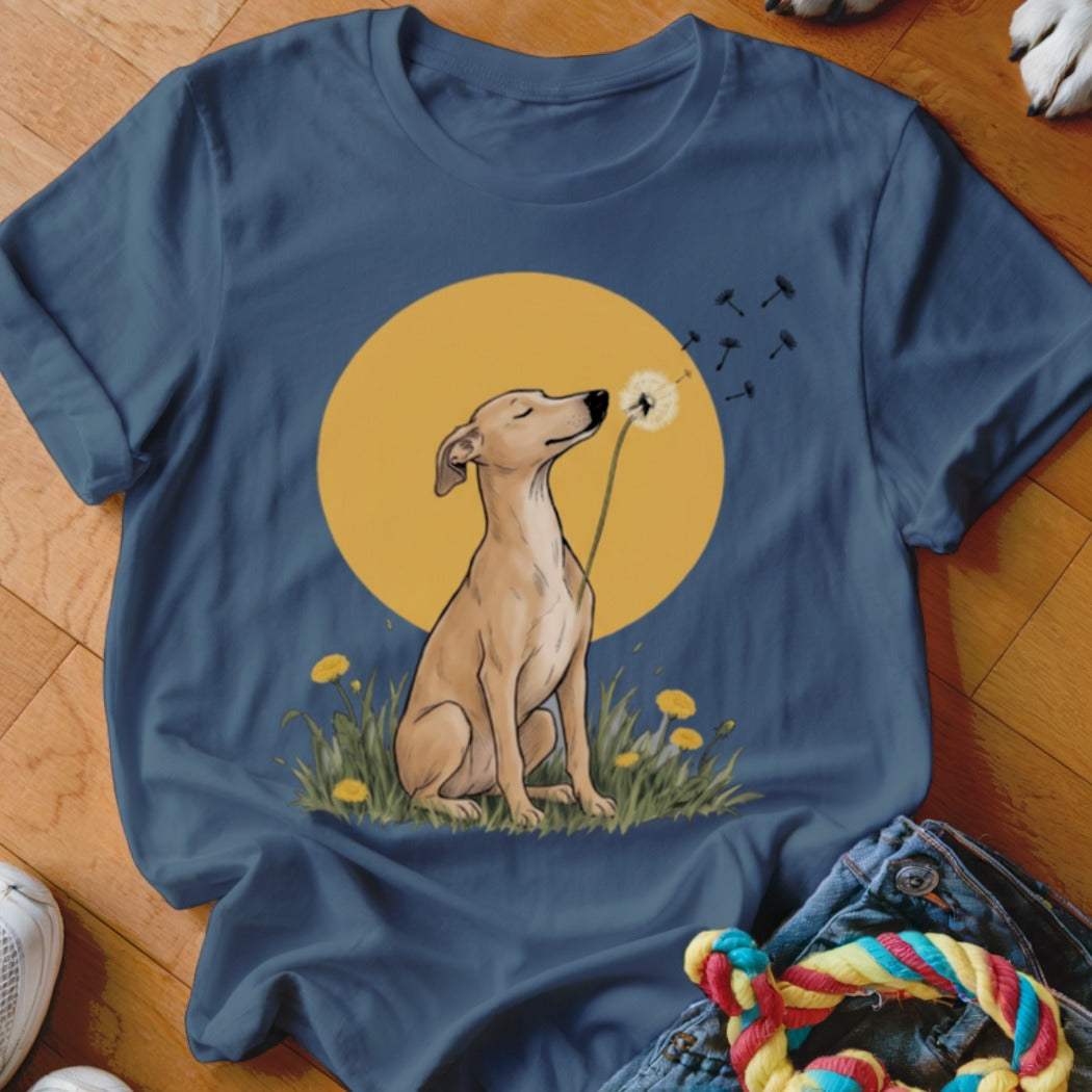 A blue t-shirt featuring an illustrated dog sitting in a field blowing dandelion seeds.