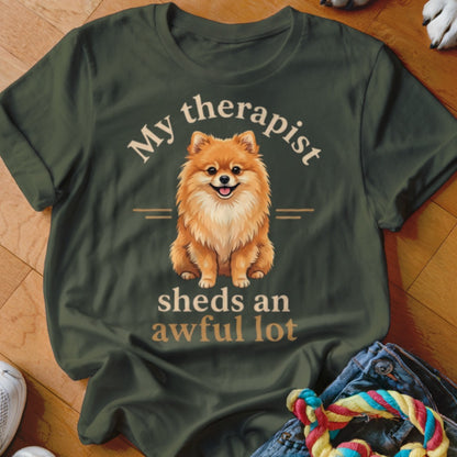 An olive green t-shirt with an illustration of a Pomeranian and the text My therapist sheds an awful lot.