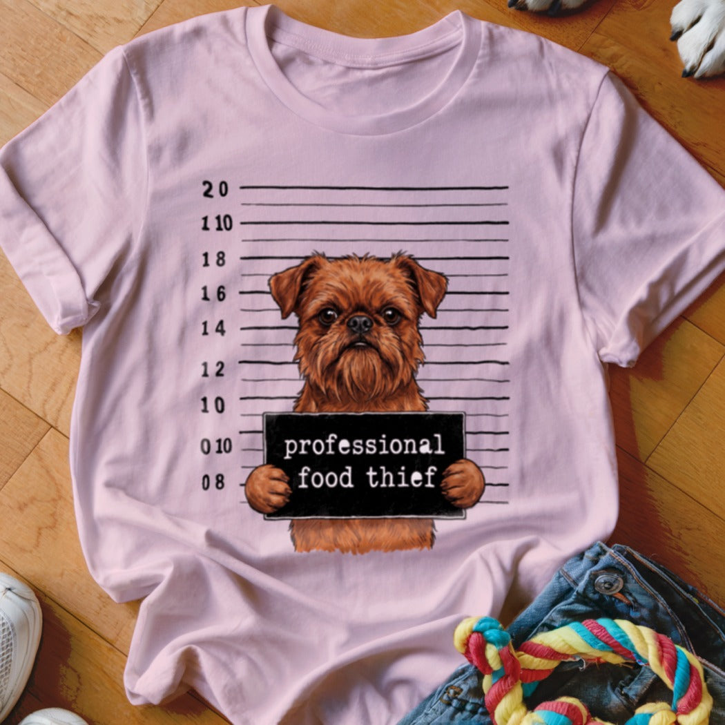 Brown dog in mugshot with sign reading "professional food thief" on a pink t-shirt.